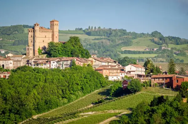 Borgo medievale con castello domina colline verdi e vigneti, un paesaggio tipico delle Langhe e Monferrato.