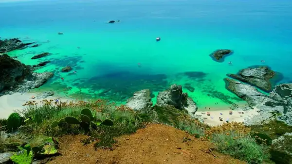 Vista dall'alto di una baia con acqua cristallina e spiagge dorate, tra le spiagge più belle della Calabria. Rocce e vegetazione mediterranea incorniciano il paesaggio.