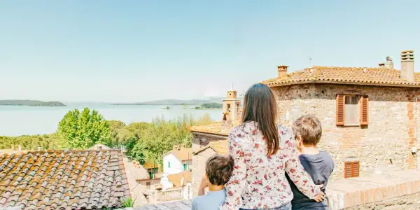 Una madre e due bambini ammirano un lago e un borgo italiano, scoprendo luoghi magici per bambini in Italia.