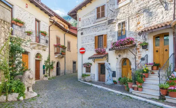 Cobblestone street in a medieval Italian village with stone buildings, balconies, and potted flowers.