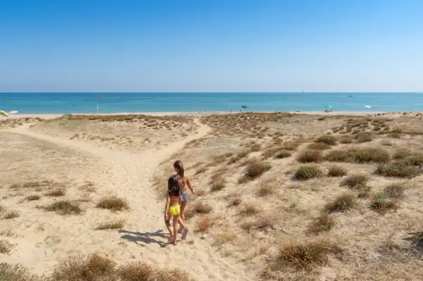 Due bambine corrono verso il mare in Abruzzo, tra dune sabbiose e macchia mediterranea.