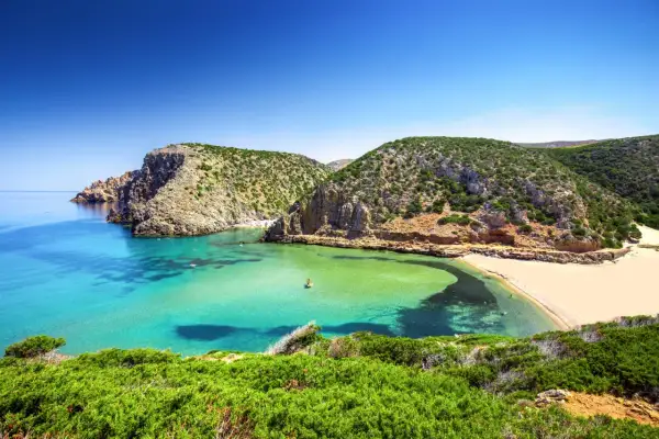 Spiagge della Sardegna: caletta con acque cristalline, sabbia dorata e macchia mediterranea. Un angolo di paradiso che risponde alla domanda: quali sono le spiagge più belle della Sardegna?