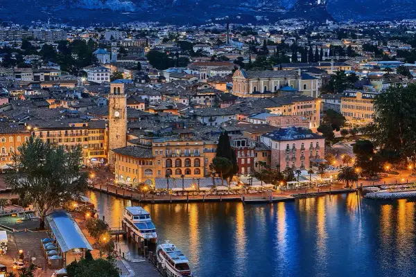Incantevole vista serale di un borgo sul lago, con edifici colorati, un campanile e barche illuminate. Un gioiello tra i paesi del Trentino Alto Adige.