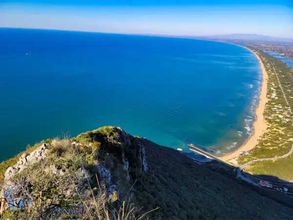 Vista dall'alto del promontorio del Circeo, con il mare azzurro, la spiaggia dorata e la vegetazione lussureggiante.