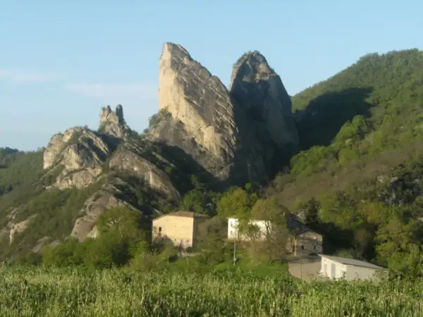 I Sassi di Roccamalatina, imponenti formazioni rocciose, dominano un paesaggio verdeggiante con casolari sparsi.
