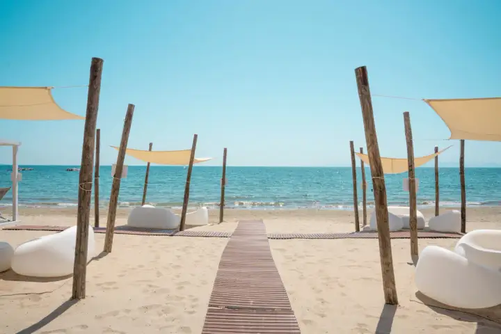 Un percorso in legno conduce al mare cristallino del golfo di Follonica, tra comode sedute bianche e tende parasole.